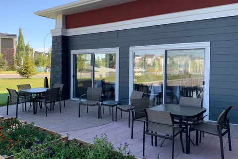 Patio with tables and chairs beside large windows and a flower bed