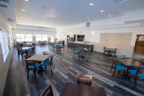 Dining room with tables, teal chairs, large windows and a serving counter