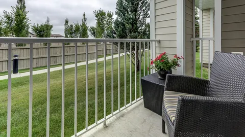 Patio with a wicker chair, a flower planter and a railing beside a lawn