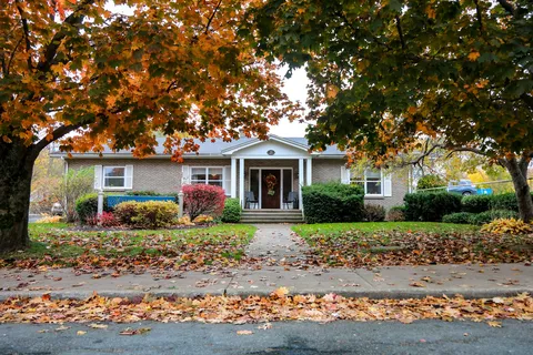 Brick building with a front lawn and trees with autumn leaves
