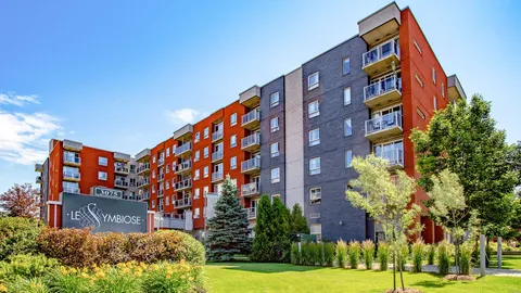 Red brick and grey residential building with balconies, lawn, shrubs and a freestanding sign