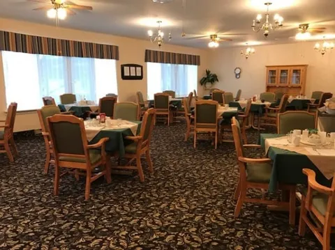 Dining room with tables, green chairs and patterned carpeting.
