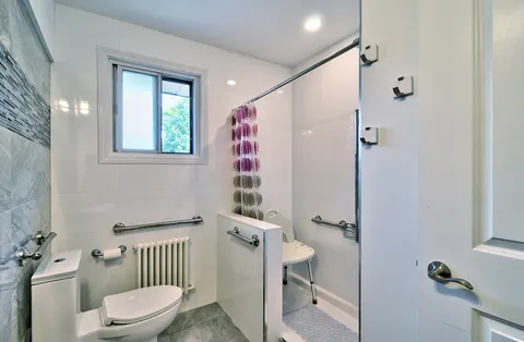 Bathroom with a toilet, shower chair, grab bars and a window