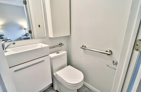 Bathroom with a white vanity, toilet, mirror and metal grab bars