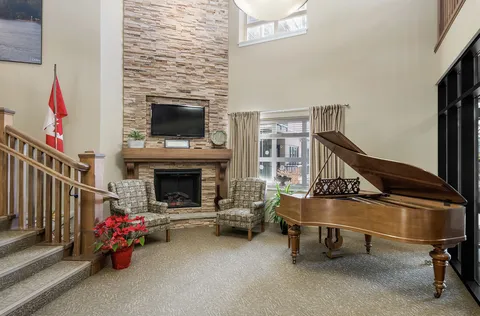 Grand piano and armchairs beside a fireplace and tall stone wall