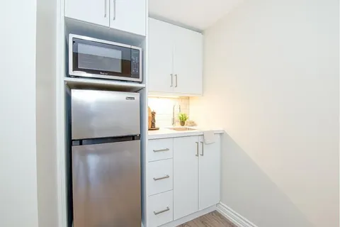 Kitchenette with white cabinets, sink, microwave and refrigerator.