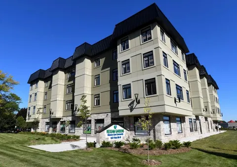 Multi-storey residence with a stone base and a sign beside the lawn.