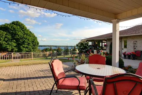Covered patio with a round table, red chairs, flowers and a view of the water.