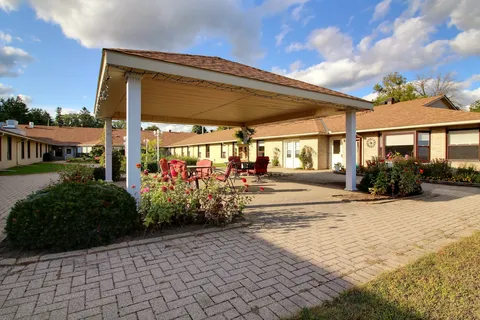 Covered patio entrance with red chairs, flower beds and a paved walkway.