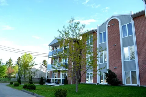 Brick residence with balconies, windows, trees and a lawn.