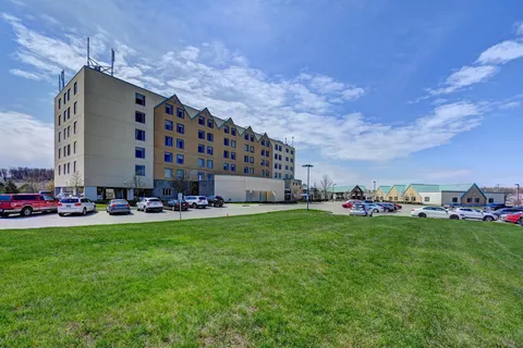 Six-storey residence beside parking areas, lawns and adjoining low-rise buildings.