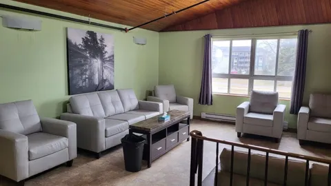 Room with grey armchairs, a sofa, coffee table, woodland artwork and a large window