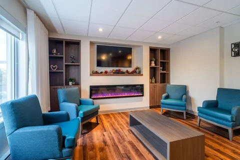 Common room with blue armchairs, a television and a fireplace.