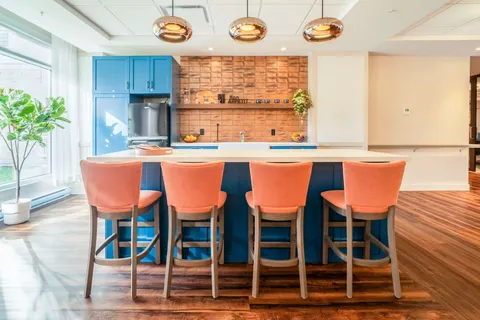 Communal kitchen with a blue island and orange stools.