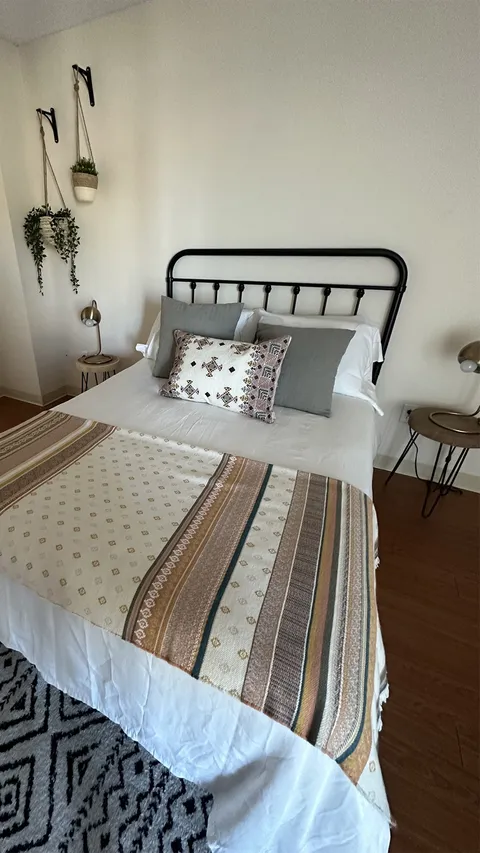 Bedroom with a metal bed frame, striped bedspread and hanging plants.