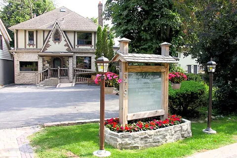 Two-storey house with a covered porch behind a sign and flower beds
