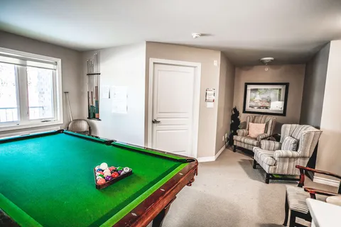 Room with a green pool table, patterned armchairs and a window