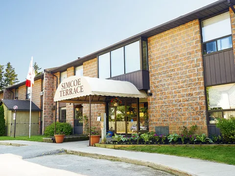 Residence entrance facade with a white awning, flower beds and Canadian flag.