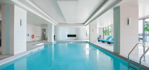Indoor pool with metal handrails and blue loungers beside tall windows