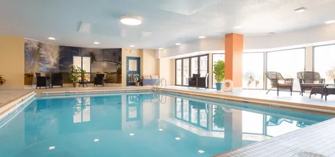 Indoor pool beside large windows, wicker chairs and a tropical landscape mural