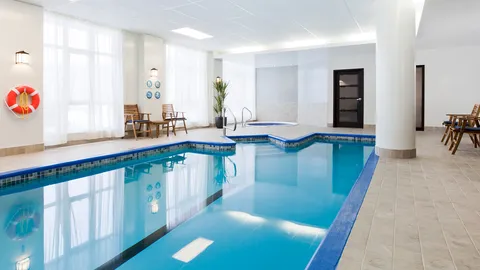Indoor swimming pool and hot tub with chairs beside tall windows