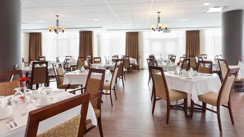 Dining tables with white linens and upholstered chairs beside curtained windows