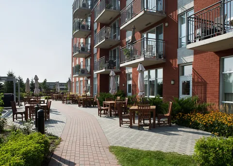 Brick residence with balconies beside a paved patio lined with tables and umbrellas