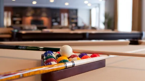 Billiard balls and cue on a table, with another table behind