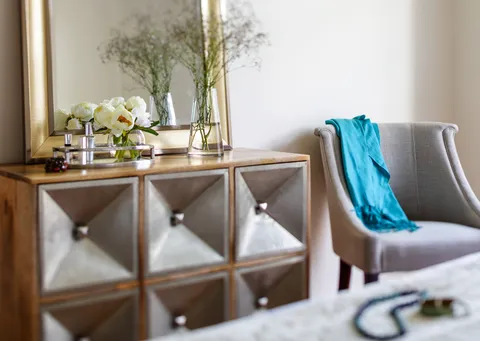 Armchair with a blue throw beside a mirrored cabinet and flowers