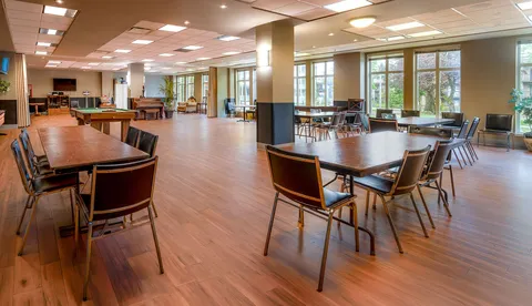 Large common hall with wooden tables, chairs and broad windows.