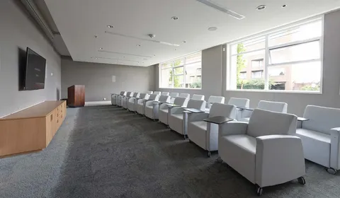 Rows of armchairs facing a television beside large windows