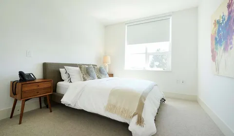 Bedroom with white bedding, a bedside drawer and colourful abstract artwork