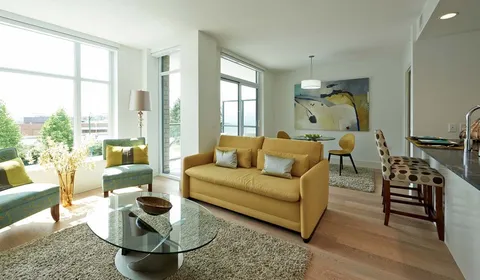 Sofa and armchairs around a glass coffee table beside windows and a kitchenette