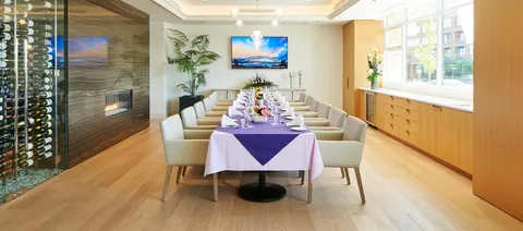 Long dining table with a purple runner beside a fireplace and windows