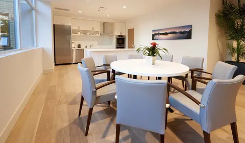 Chairs around a round table beside cupboards, a sink and landscape artwork