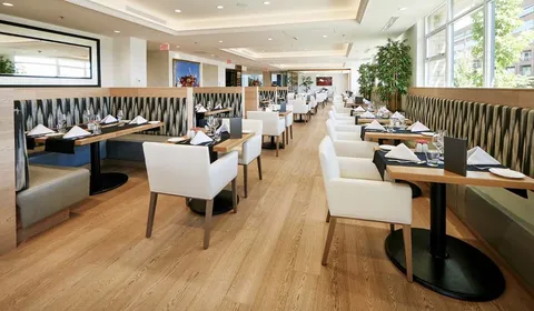 Dining tables set with glasses beside striped bench seating and large windows