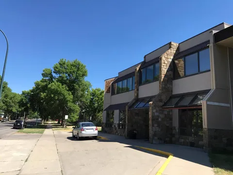 Residence with stone walls and large windows beside a sidewalk and parked car