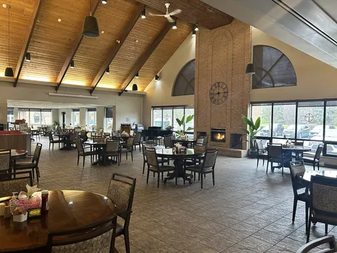 Dining room with round tables, fireplace, grand piano and timber ceiling.