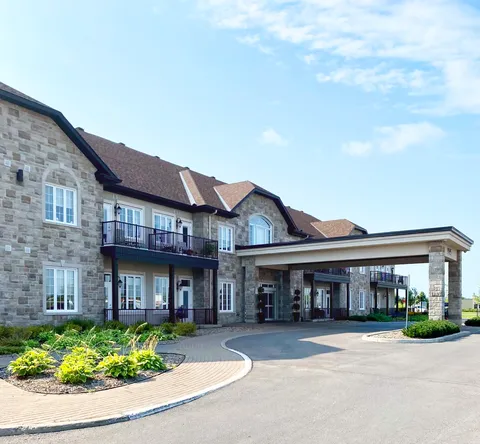 Stone-faced building with balconies, a covered entrance and landscaped flower beds