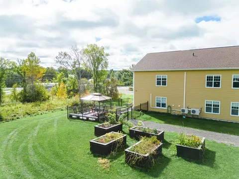 Raised garden beds and a deck beside the yellow residence