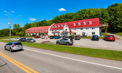 White residence with a red roof, parking area and wooded hillside