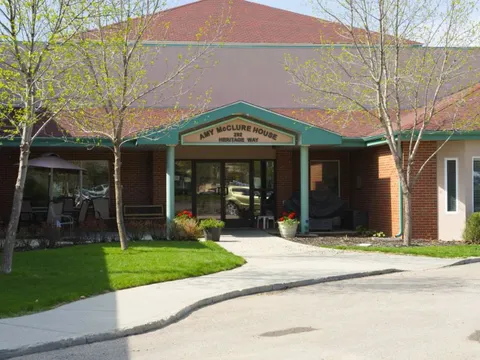 Brick residence entrance with a green canopy, flowerpots, benches and a lawn