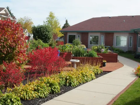 Garden with raised beds, shrubs, a birdbath and a paved path beside a brick residence