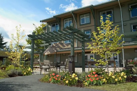 Residence building beside a pergola, patio seating and flower beds