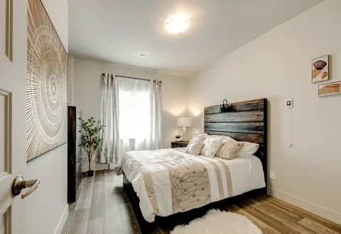 Bedroom with a wooden headboard, pale bedding, a bedside lamp and a window