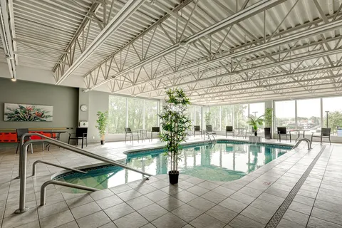 Indoor swimming pool with windows, deck chairs and a high metal ceiling