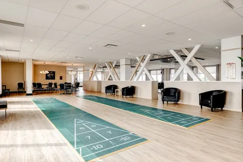 Indoor shuffleboard courts beside black chairs and broad windows