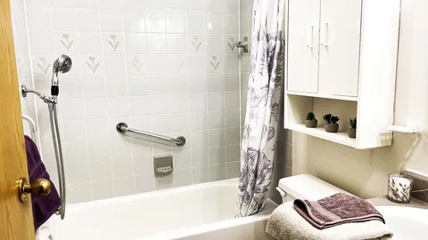 Bathroom with a bathtub, handheld shower, grab bar and white cabinet