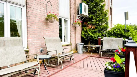 Patio with garden chairs, small tables and flower planters beside a brick wall