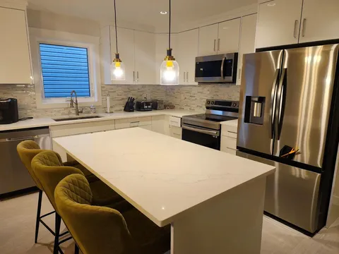Shared kitchen with white cabinets, an island, stools and stainless steel appliances.